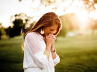 a young woman praying in a park