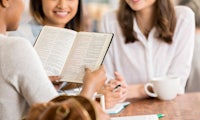 three women sitting around a table reading a bible