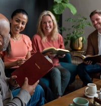 a group of people sitting around a coffee table and reading a bible