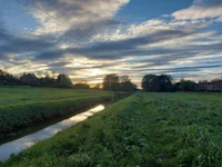 the sun is setting over a grassy field with a stream running through it